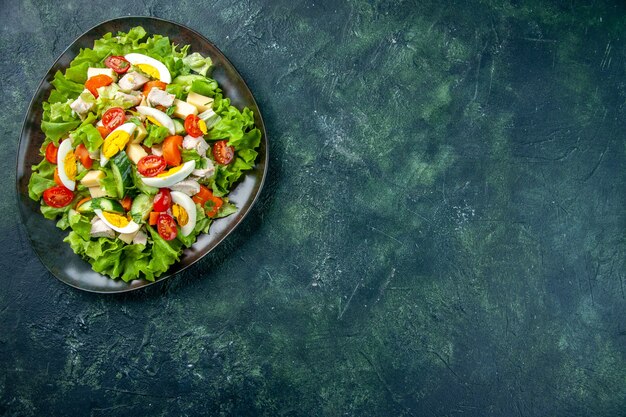 Boven weergave van zelfgemaakte heerlijke salade in een zwarte plaat aan de rechterkant op groen zwart mix kleuren tafel met vrije ruimte