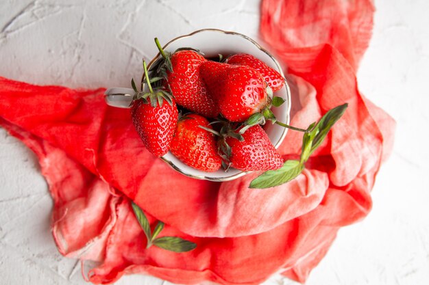 Bovenaanzicht aardbeien in koffiekopje op rode doek op witte achtergrond. horizontaal