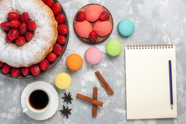 Bovenaanzicht aardbeientaart met suikerpoeder en macarons op wit