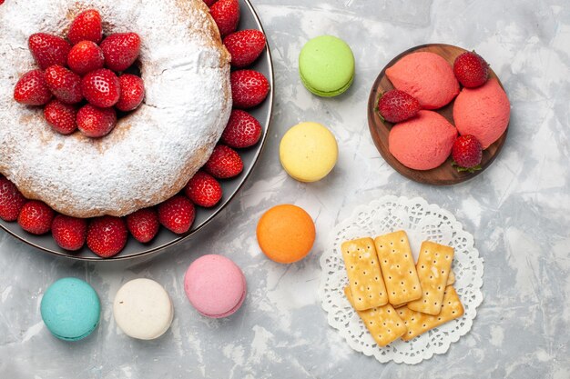 Bovenaanzicht aardbeientaart met verse aardbeien en macarons op licht-wit