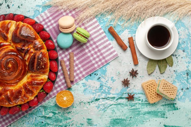 Bovenaanzicht aardbeientaart met wafels Franse macarons en kopje thee op blauwe ondergrond