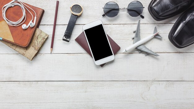 Bovenaanzicht accessoires om te reizen concept.White mobiele telefoon en koptelefoon op houten background.airplane, kaart, paspoort, kijk op houten tafel.