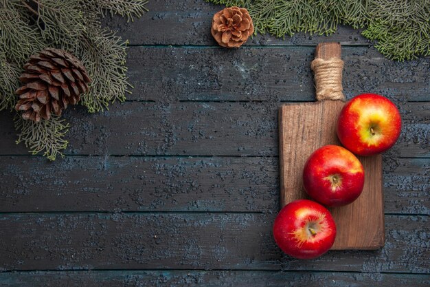 Bovenaanzicht appels aan boord van drie appels op houten snijplank onder takken met kegels