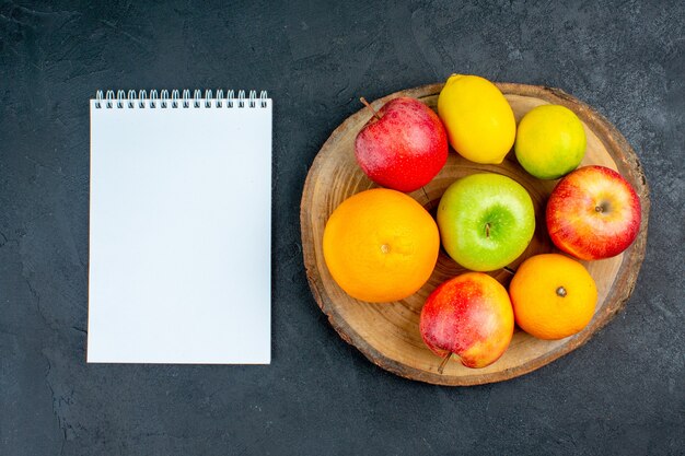 Bovenaanzicht appels citroen sinaasappelen op houten bord een notebook op donkere ondergrond