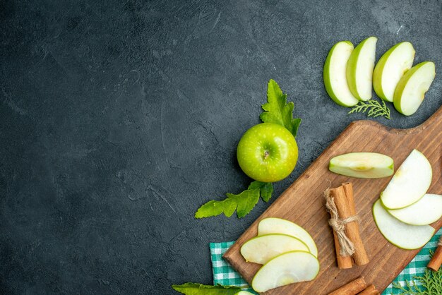 Bovenaanzicht appelschijfjes en kaneel op snijplank gedroogd muntpoeder in kleine kom appel op zwarte achtergrond