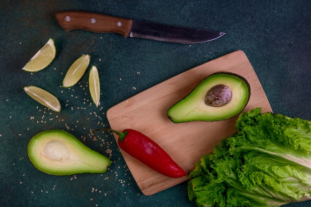 Bovenaanzicht avocado helften op een schoolbord met citroen rode paprika sla en mes op een donkergroene achtergrond