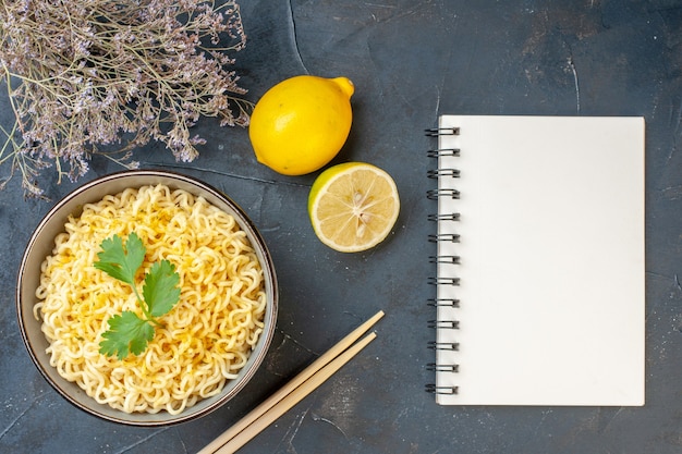 Bovenaanzicht aziatische ramen noedels in kom citroen en gesneden citroen eetstokjes notitieboekje op donkere tafel