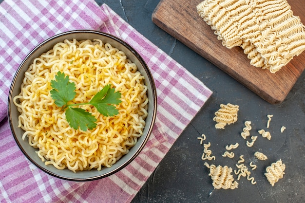 Bovenaanzicht Aziatische ramen noedels in kom op roze wit geruit tafelkleed rauwe ramen noedels op snijplank op donkere achtergrond