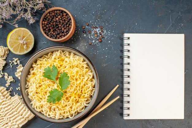 Bovenaanzicht aziatische ramen noedels in kom zwarte peper in kleine kom gesneden citroen eetstokjes notitieblok op donkere tafel