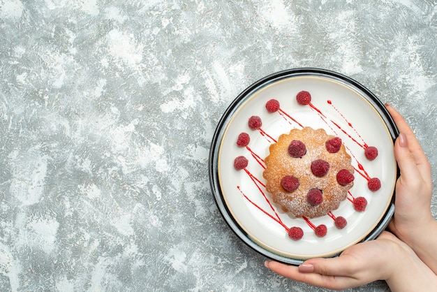 Bovenaanzicht bessencake op witte ovale plaat in vrouwelijke hand op grijze oppervlakte vrije plaats