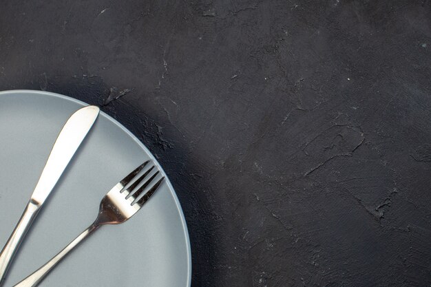 Bovenaanzicht blauw bord met mes en vork op donkere ondergrond