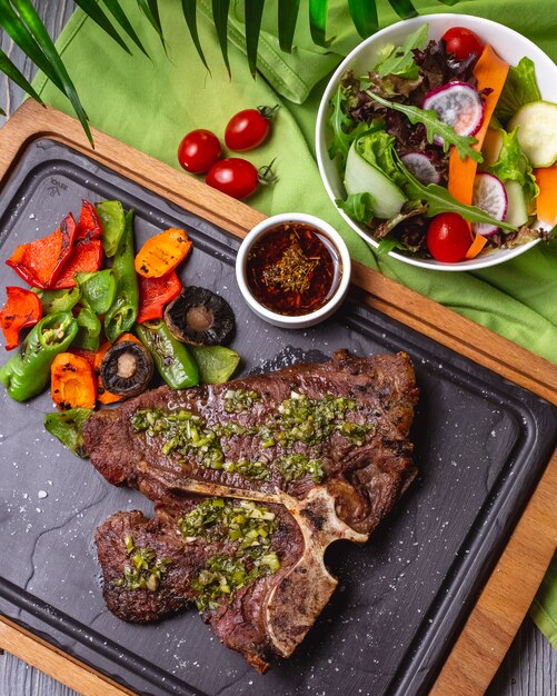 Bovenaanzicht bone steak met gegrilde groenten en saus op het bord met groente salade