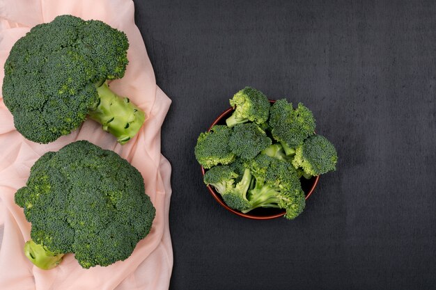 Bovenaanzicht bos van broccoli op roze doek met broccoli in keramische kom