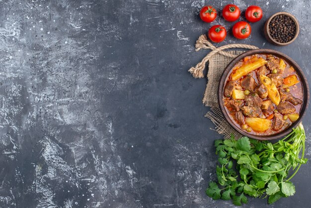 Bovenaanzicht bozbash vleessoep in houten kom koriander tomaten zwarte peper in kleine kom op grijze tafel met kopieerruimte