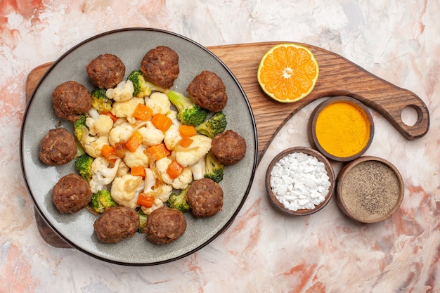 Gratis foto bovenaanzicht broccoli en bloemkool salade en gehaktbal op plaat op snijplank verschillende kruiden in kleine kommen op naakt geïsoleerde achtergrond