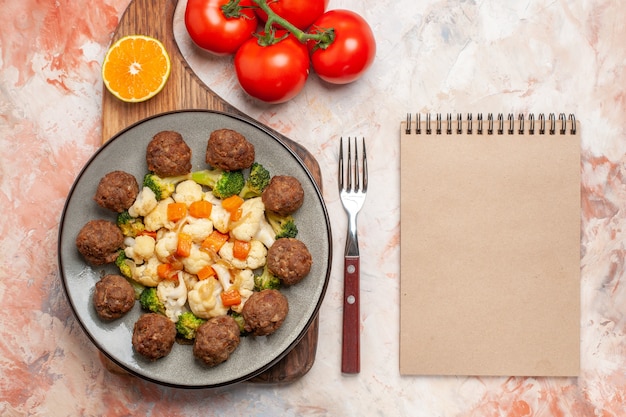 Gratis foto bovenaanzicht broccoli en bloemkool salade en gehaktbal op plaat schijfje citroen op snijplank een vork tomaten een notitieblok op naakt geïsoleerde achtergrond