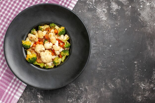 Bovenaanzicht broccoli en bloemkoolsalade op zwart bord roze en wit geruit tafelkleed op donkere oppervlakte vrije ruimte