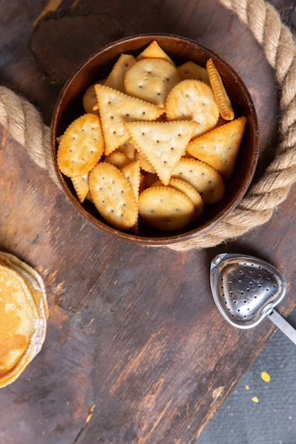Bovenaanzicht bruine plaat met crackers en pannenkoeken op de houten foto van het de maaltijdontbijt van het bureauvoedsel