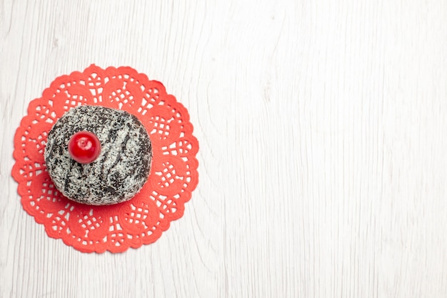 Bovenaanzicht cacaocake met zure kers op het rode ovale kanten kleedje op de witte houten tafel