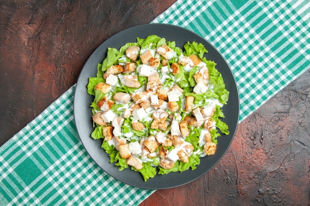 Gratis foto bovenaanzicht caesarsalade op ovale plaat groen wit geruit tafelkleed op donkere tafel