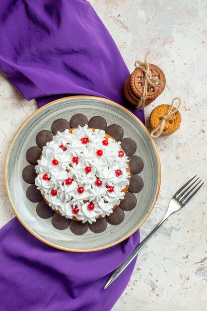 Gratis foto bovenaanzicht cake met banketbakkersroom op ovale plaat paarse sjaalkoekjes vastgebonden met touwvork op grijze tafel