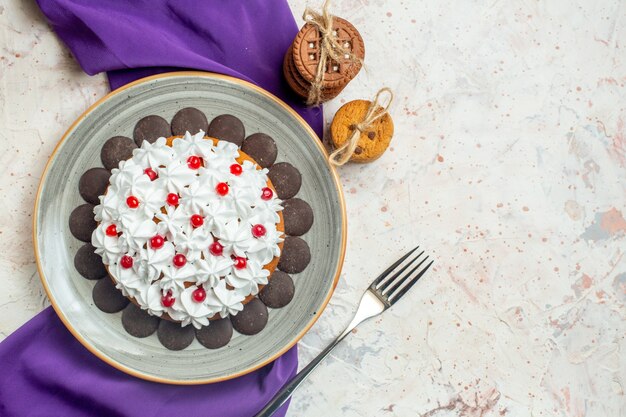 Bovenaanzicht cake met banketbakkersroom op ovale plaat paarse sjaalkoekjes vastgebonden met touwvork op witte tafel