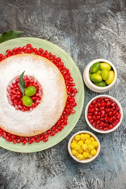 Bovenaanzicht cake met granaatappel drie kommen bessen een bord cake met granaatappel