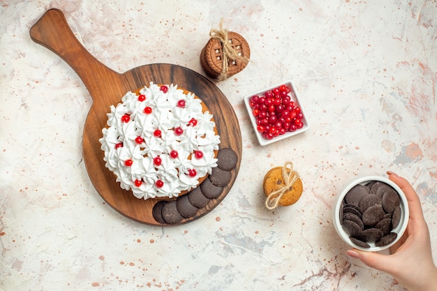 Bovenaanzicht cake met witte banketbakkersroom op snijplankkom met bessenchocoladekom in vrouwelijke handkoekjes vastgebonden met touw op lichtgrijze tafel