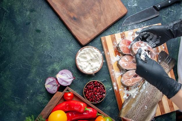 Bovenaanzicht chef-kok die rauwe visplakken bedekt met bloem, verse groenten op een houten bord, meelkom, mes op de keukentafel, vrije ruimte