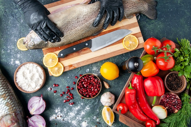 Gratis foto bovenaanzicht chef-kok met zwarte handschoenen met rauwe vis op een houten bord pepermolen meelkom granaatappel zaden in kom op tafel