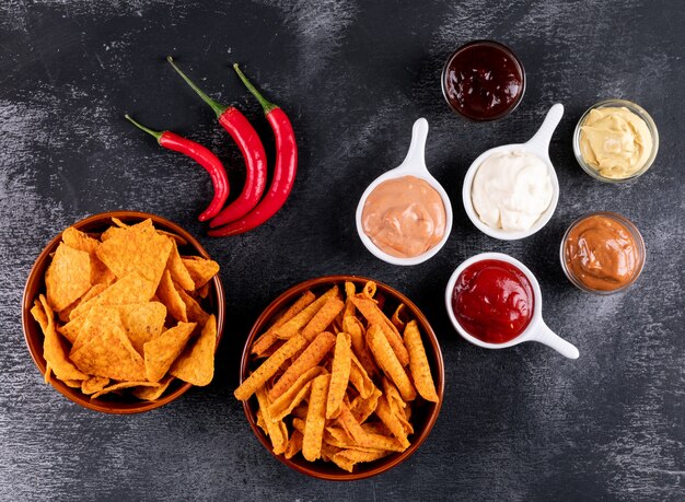 Bovenaanzicht chips met chili peper en sauses in kommen op zwarte steen horizontaal