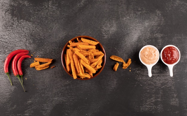 Bovenaanzicht chips met chili peper en sauses in kommen op zwarte steen