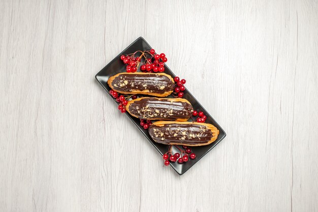 Bovenaanzicht chocolade-eclairs en krenten op de zwarte rechthoekige plaat in het midden van de witte houten ondergrond