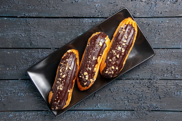 Bovenaanzicht chocolade eclairs op rechthoek plaat op donkere houten tafel met vrije ruimte