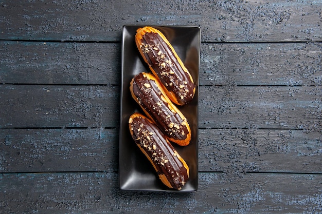 Bovenaanzicht chocolade-eclairs op rechthoekige plaat in het midden van de donkere houten tafel met vrije ruimte