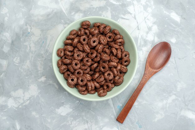 Bovenaanzicht chocolade granen in groene plaat samen met hout, lepel op blauw, ontbijtgranen cornflakes cacao