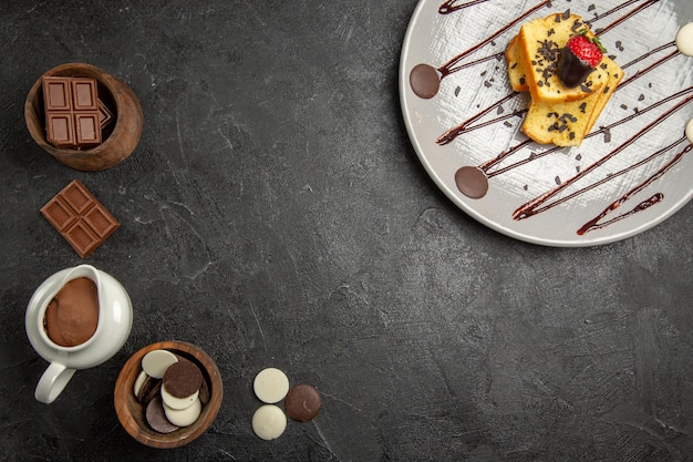 Bovenaanzicht chocolade op tafel chocolade en chocoladeroom aan de linkerkant en een bord smakelijke cake met chocolade en aardbeien aan de rechterkant van de zwarte tafel