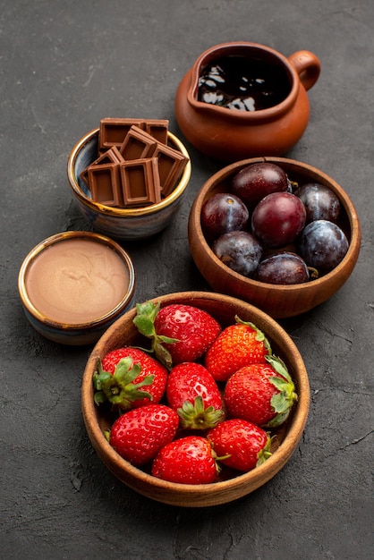 Bovenaanzicht chocoladebessen houten kommen aardbeien chocoladebessen en chocoladesaus in het midden van de donkere tafel