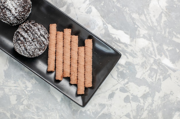 Gratis foto bovenaanzicht chocoladecake met zoete pijpkoekjes in zwarte plaat op wit oppervlak