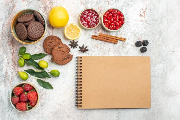 Bovenaanzicht chocoladekoekjes crème notitieboekje chocoladekoekjes kommen met bessen citrusvruchten kaneelstokjes op tafel