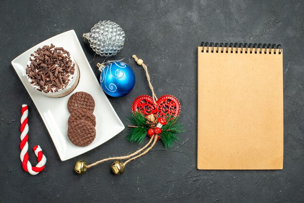 Bovenaanzicht chocoladetaart en koekjes op witte rechthoekige plaat kerstboom speelgoed een notitieblok op donkere geïsoleerde achtergrond