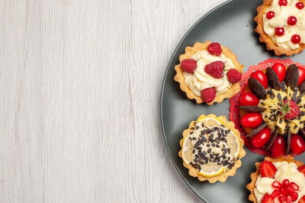 Bovenaanzicht chocoladetaart rechts boven afgerond met bessentaartjes in de grijze plaat op de witte houten tafel