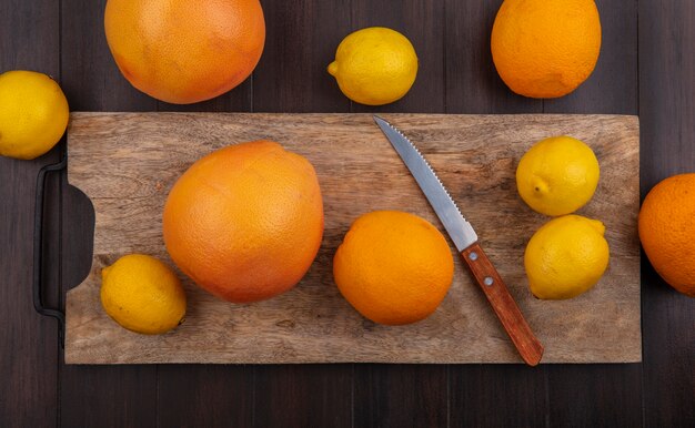 Bovenaanzicht citroenen met sinaasappelen en grapefruit op een snijplank met een mes op een houten achtergrond