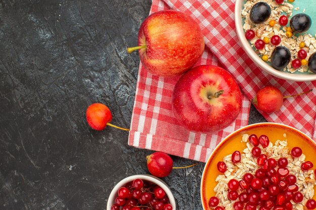 Bovenaanzicht close-up bessen twee appels kommen rode aalbessen kersen druiven havermout granaatappel