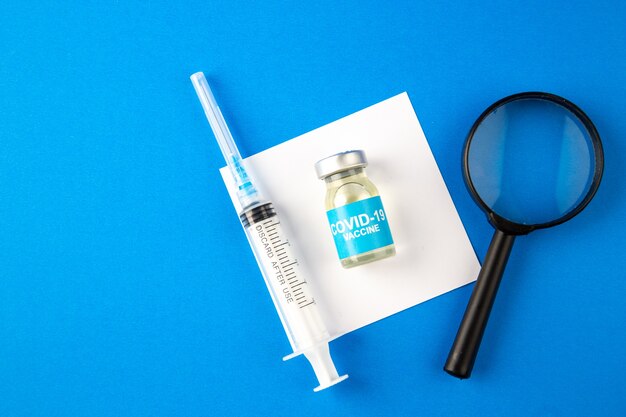 bovenaanzicht Covid-vaccin met vergrootglas en injectie op blauwe achtergrond Ziekenhuisgezondheid Covid-Lab pandemisch virusgeneesmiddel
