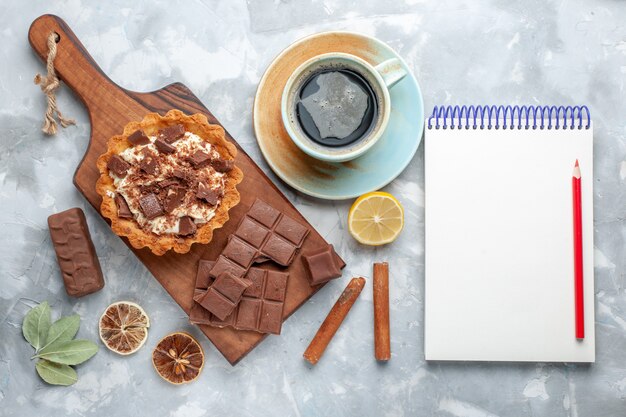 Bovenaanzicht crème kleine cake met chocoladerepen en thee op licht bureau zoete cake suiker chocolade