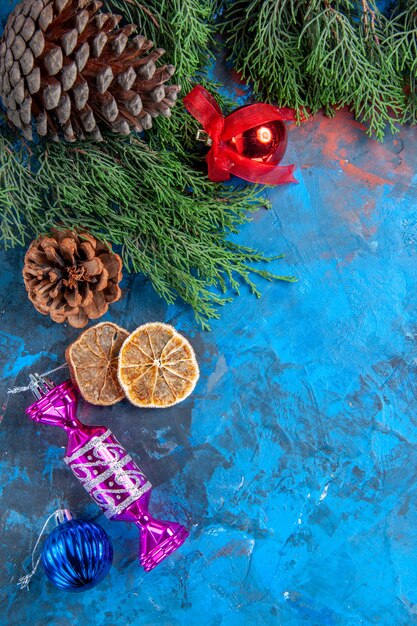 Bovenaanzicht dennenboom takken dennenappels kerstboom speelgoed gedroogde schijfjes citroen op blauw-rood oppervlak
