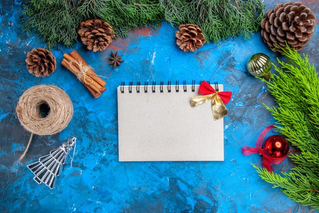 Bovenaanzicht dennenboom takken stro draad kaneelstokjes anijs zaden kerstboom ballen een notitieboekje met strik op blauw-rode achtergrond