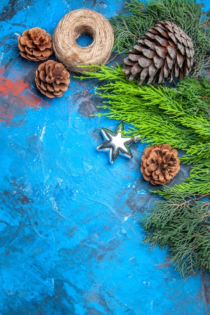 Bovenaanzicht dennenboomtakken met dennenappels stro draad op blauw-rood oppervlak