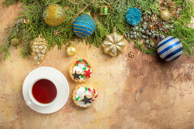 Bovenaanzicht dennentakken kerstboom versieringen een kopje thee cupcakes op beige achtergrond